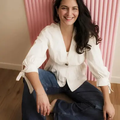 Julie assise devant un rideau rose, souriante.